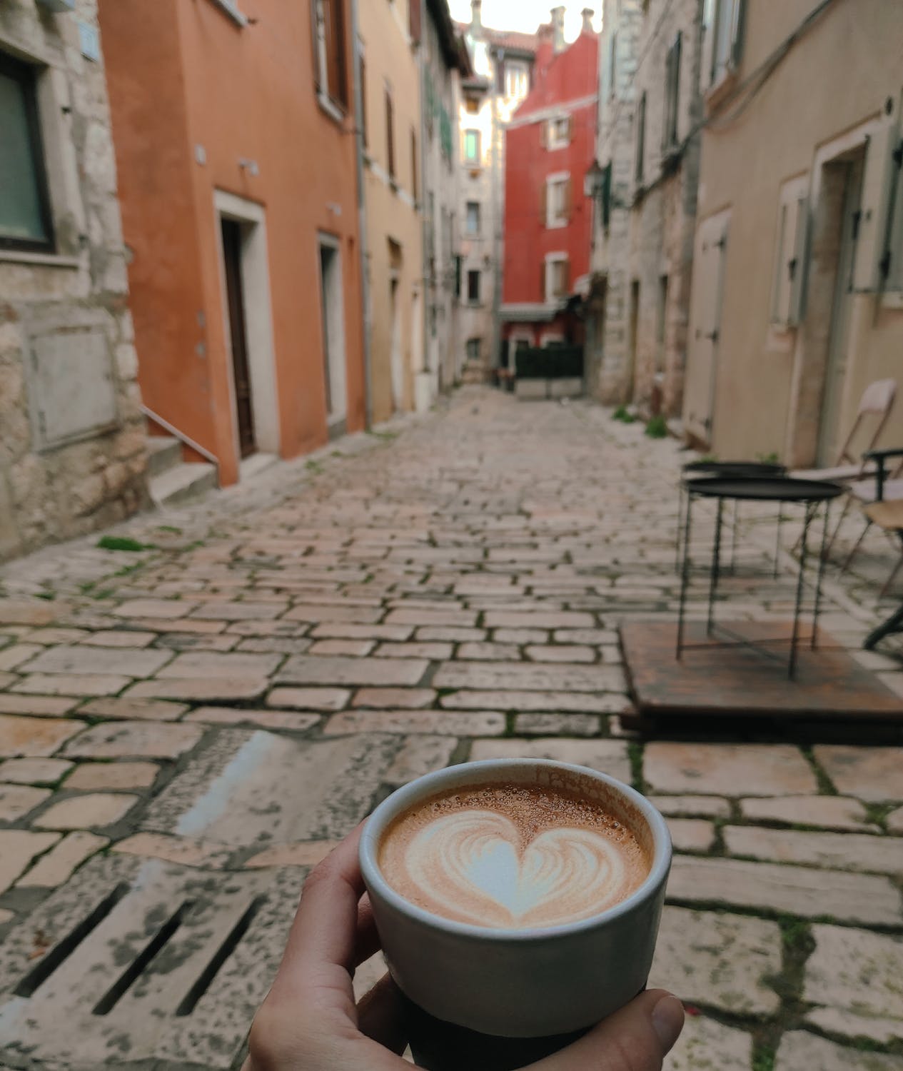 free-photo-of-a-person-holding-a-cup-of-coffee-in-front-of-a-cobblestone-street